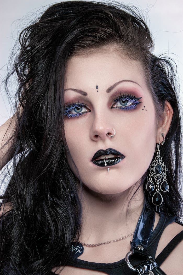 Home Close-up portrait of a woman with gothic makeup, unique accessories, and striking black hair.