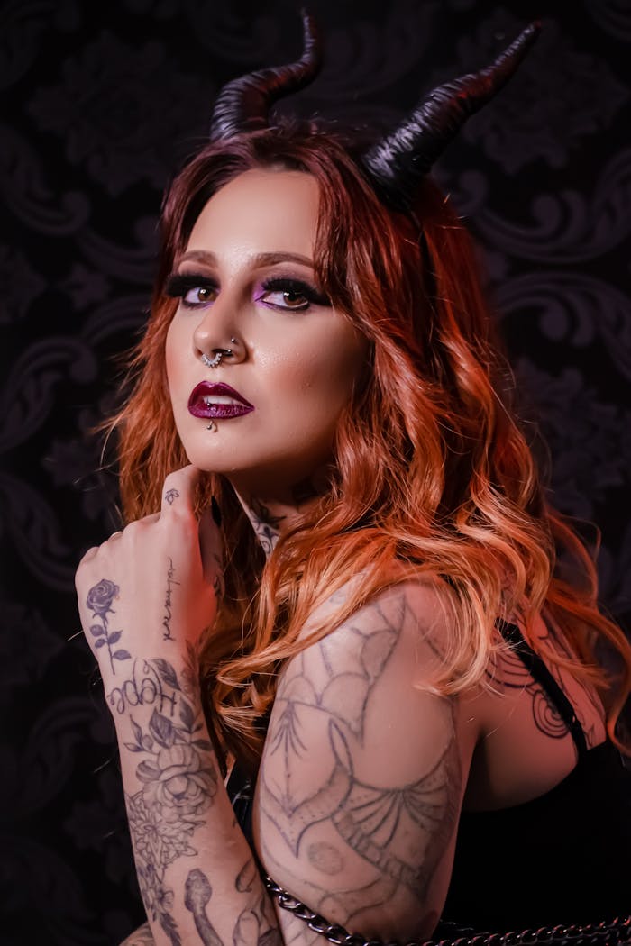 A glamorous portrait of a young woman with devil horns and intricate tattoos.