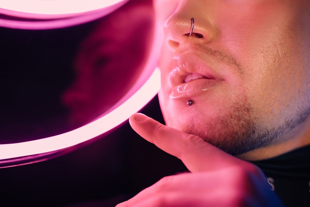 A stylish close-up of a person with lip and nose piercings under neon lighting.