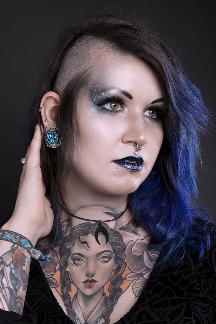 Home Artistic portrait of a woman with tattoos and bold cosmic-themed makeup in a studio setting.