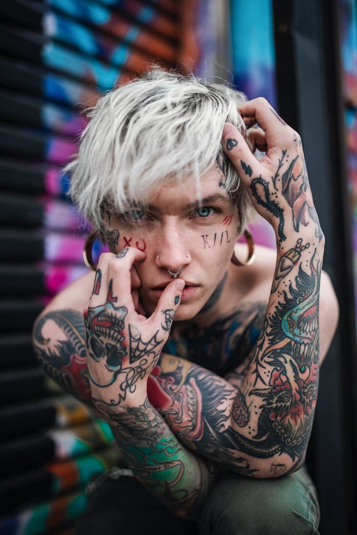 Intense portrait of a tattooed person with piercings and a contemplative expression, featuring street art background.