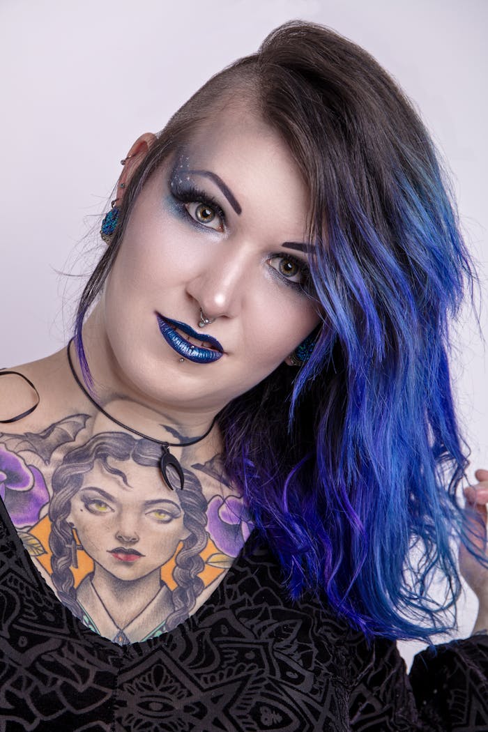 About A striking portrait of a woman showcasing vibrant blue hair and unique tattoos in a studio setting.